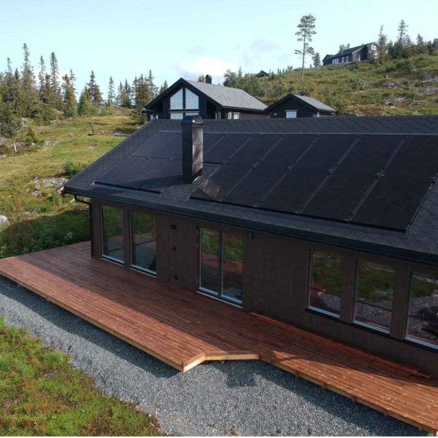 Ny og moderne brunsvart hytte med sort tak med innfelt solcellepanel.